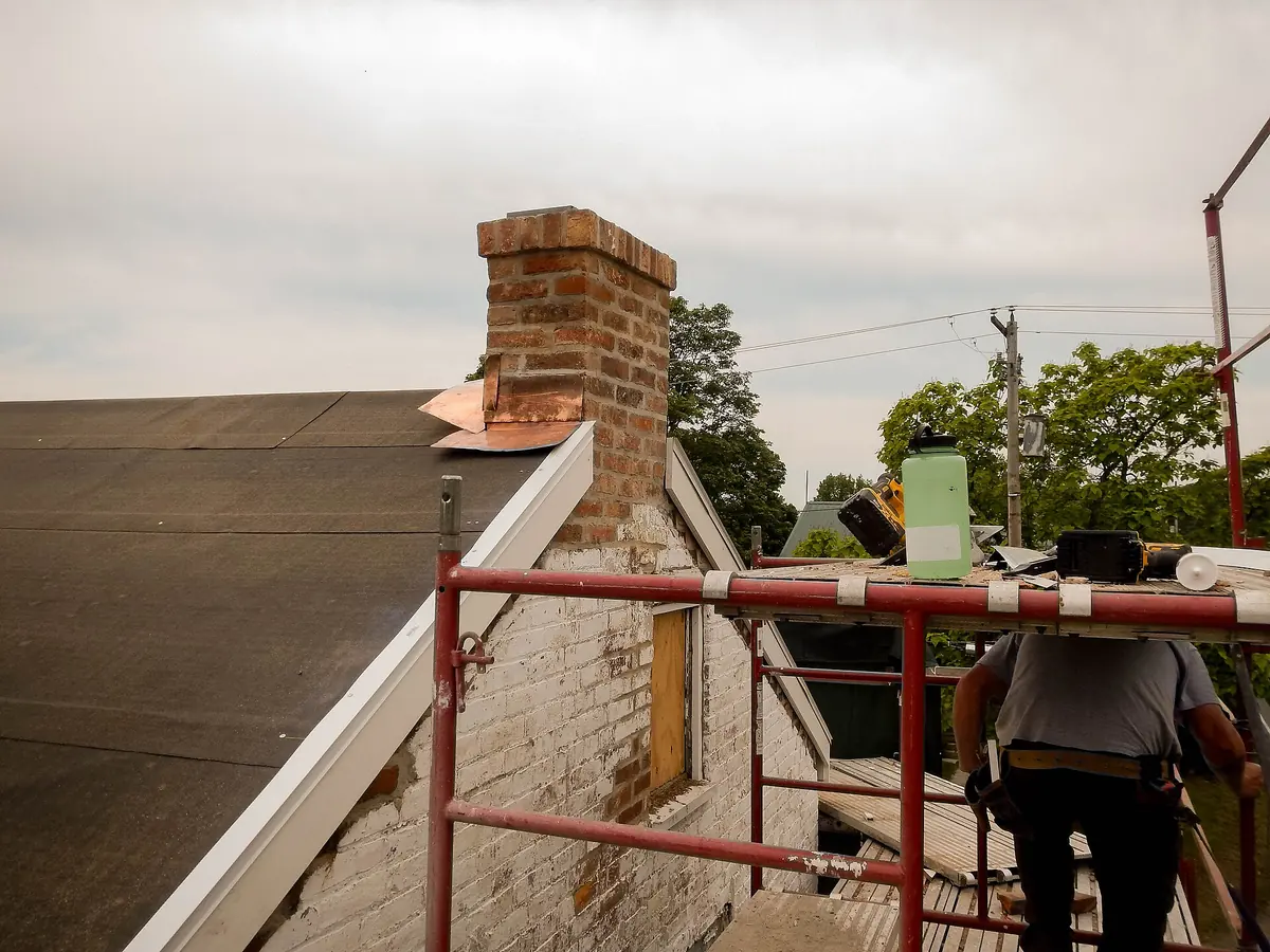 A mason on scaffolding fitting new copper flashing around a rebuilt brick chimney